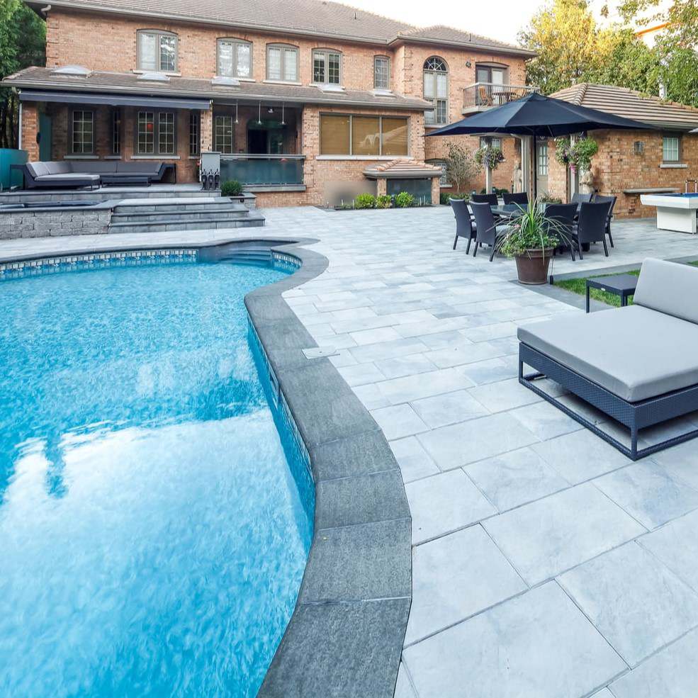 Dark basalt coping following the curve of a freeform pool, with light paving