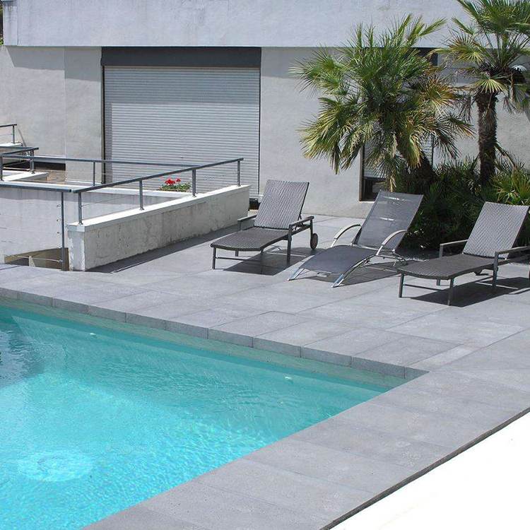 Light grey basalt coping and terrace tiles around an outdoor swimming pool