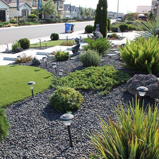 Black basalt gravel used as mulch in a front-yard rock garden with path lights
