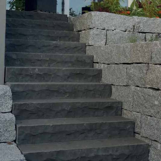 Long run of black basalt stair treads beside a dry-stone retaining wall